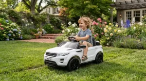 A toddler navigating a white 12V electric ride-on car for toddlers around backyard garden beds.